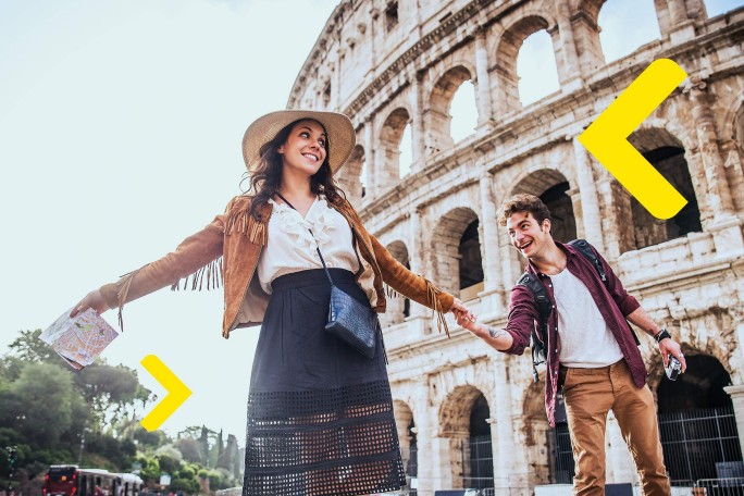 Doua persoane stau in fata Colosseumului din Roma, Italia. Persoana din stanga poarta o palarie, o jacheta maro cu franjuri si o fusta neagra cu un top alb. Persoana din dreapta poarta o camasa rosie peste un tricou alb si pantaloni maro. Ambele persoane se tin de mana. Sunt doua sageti mari galbene care indica spre ele din directii opuse.